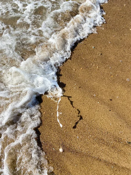 Close-up da costa do mar, água do mar clara com ondas rasas e uma estreita faixa de espuma branca com bolhas lava a costa com uma superfície de areia marrom lisa — Fotografia de Stock
