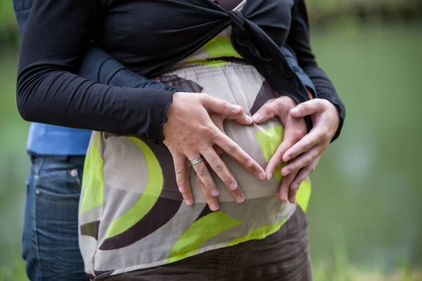 Mani di donna incinta e il suo partner femminile a forma di cuore sul suo ventre — Foto Stock