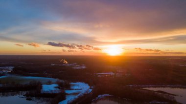 Siyah ağaç siluetleri ve gri bir yol mavi gökyüzü arka planında turuncu ve sarı gün batımlarıyla
