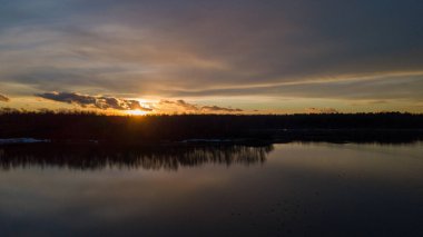 Bir orman gölü üzerinde güzel ve dramatik bir gün batımının havadan görüntüsü suya yansıyor, insansız hava aracı görüntüleri.