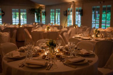 Renkli çiçeklerle süslenmiş şölen masası. Masaların üzerinde tabaklar, bardaklar, mumlar ve çatal bıçak takımı var.