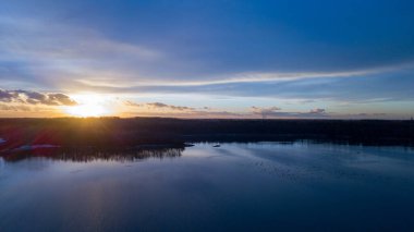 Bir orman gölü üzerinde güzel ve dramatik bir gün batımının havadan görüntüsü suya yansıyor, insansız hava aracı görüntüleri.