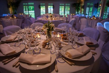 Renkli çiçeklerle süslenmiş şölen masası. Masaların üzerinde tabaklar, bardaklar, mumlar ve çatal bıçak takımı var.