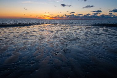 Denizde parlayan batan güneşin görüntüsü sahile yansıyor, güneş gibi parlayan bulutlar. Peyzaj