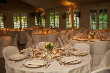 Renkli çiçeklerle süslenmiş şölen masası. Masaların üzerinde tabaklar, bardaklar, mumlar ve çatal bıçak takımı var.