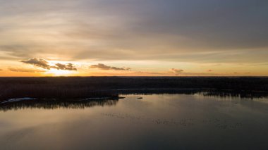 Bir orman gölü üzerinde güzel ve dramatik bir gün batımının havadan görüntüsü suya yansıyor, insansız hava aracı görüntüleri.