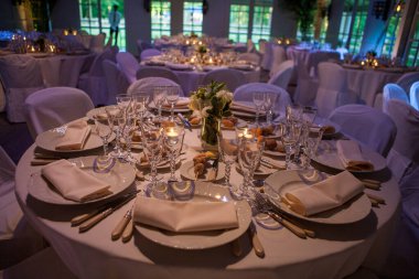 Renkli çiçeklerle süslenmiş şölen masası. Masaların üzerinde tabaklar, bardaklar, mumlar ve çatal bıçak takımı var.