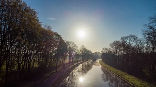 Légi kilátás egy idilli folyómeder csatorna fű bankok és vadvirágok és fák egy festői táj egy ködös napos tavaszi reggeli napkelte napon, vett egy drón — Stock Fotó