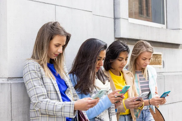 Çok ırklı bir grup güzel bayan arkadaş cep telefonları kullanarak duvarın önünde duruyorlar.