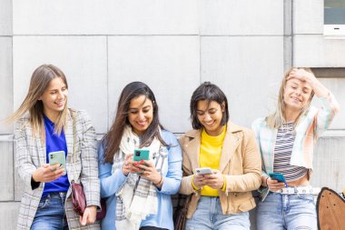 Çok ırklı bir grup güzel bayan arkadaş cep telefonları kullanarak duvarın önünde duruyorlar.