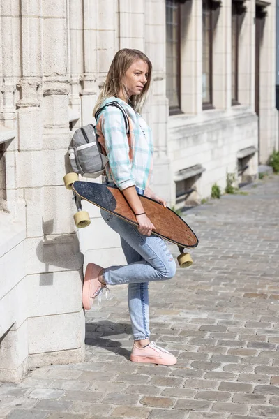 Lifestyle πορτρέτο ενός κοριτσιού φορώντας μοντέρνα ρούχα μόδας και ένα skateboard ακουμπά σε έναν τοίχο στους δρόμους της πόλης — Φωτογραφία Αρχείου