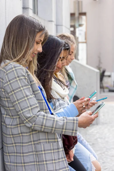Multiethnic Group of beautiful young female friends standing against a wall using mobile smartphones — Stock Photo, Image