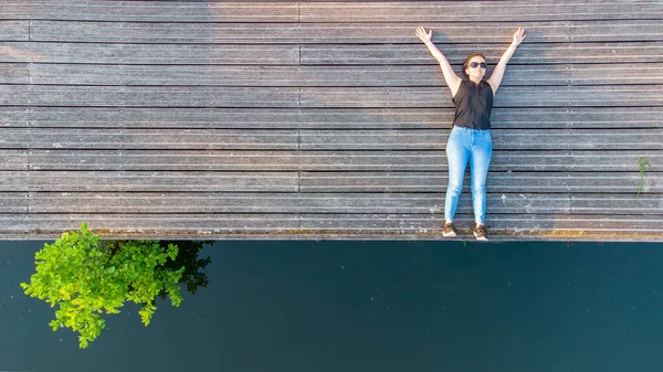 Concepto de vacaciones, disfrute y libertad. Vista aérea superior desde el retrato de estilo de vida de drones de una mujer joven a orillas de un río de madera junto al agua del río. — Foto de Stock
