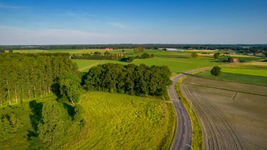 Mavi gökyüzünde tarlaları sürülen ve sürülmemiş tarlaları ve ağaçları olan dalgalı bir tarım arazisinin insansız hava aracı.