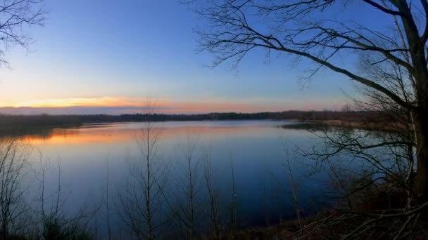 Très belle casserole horizontale d'un coucher de soleil derrière un lac calme avec mouvement de caméra lisse à travers l'herbe et les arbres sur le rivage — Video