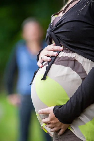 Mani di donna incinta e il suo partner femminile a forma di cuore sul suo ventre — Foto Stock