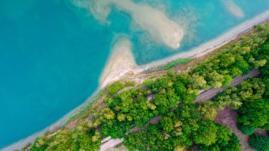 Bir orman gölünün şeffaf turkuaz suyunun baharda ağaçlarla dolu taşlı bir sahille buluştuğu güzel bir yerin havadan görünüşü. İnsansız hava aracıyla yakalandı.