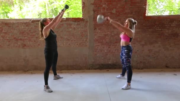 Umgeknickte Sportlerinnen in Fitnessklamotten schwingen in leerer Turnhalle Kettlebells — Stockvideo