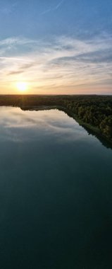 Göl kıyısında dramatik ve renkli bir gün batımının insansız hava aracı tarafından çekilen hava panoramik görüntüsü. Doğa manzarası. Avrupa 'da doğa. Yansıma, mavi gökyüzü ve sarı güneş ışığı. peyzaj