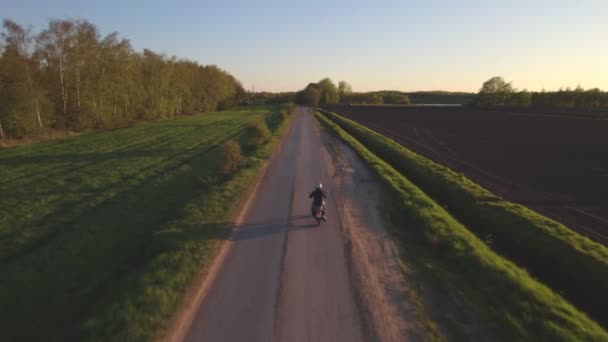 Вид з повітря, зроблений з безпілотника мотоциклів, що їздять по прямій дорозі десь у сільській місцевості між фермерськими полями на заході сонця — стокове відео