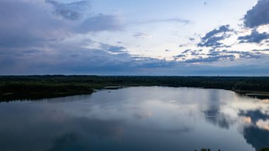 Dramatik bir günbatımı gökyüzünün altında suya yansıyan güzel bir göl manzarası. Doğa ve Seyahat Turizmi.