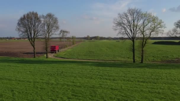 Eine Drohne schießt, ein Traktor zieht einen leeren Anhänger über einen Feldweg, der die Felder überquert. Auf dem Weg über eine große Plantage in der sonnigen Landschaft auf einen Traktor zufliegen. — Stockvideo