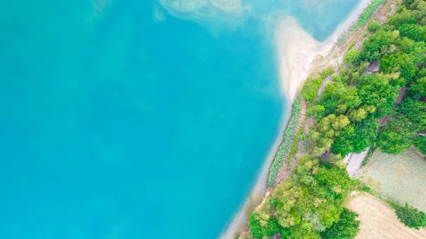 Vista aérea de um lugar pitoresco onde a água azul-turquesa transparente de um lago florestal encontra uma costa pedregosa com árvores na primavera. capturado com um drone — Fotografia de Stock