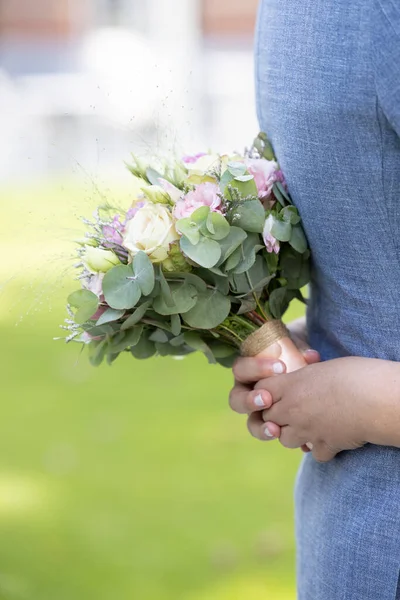Крупным планом руки невесты с букетом белых и розовых роз, которые охватывают жениха синий жилет на фоне луга — стоковое фото