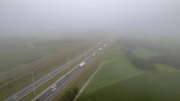 Aerial view of the road between farm fields and plantations under a grey misty sky, shot with a drone