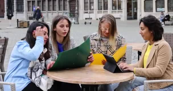 Lifestyle portret van een diverse multi-etnische groep van vier jonge glimlachende zakenvrouwen met smartphones, notities en notities buiten in een café op het werk terwijl ze iets drinken — Stockvideo