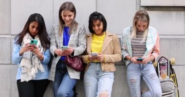 Çok ırklı bir grup güzel bayan arkadaş cep telefonları kullanarak duvarın önünde duruyorlar.