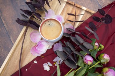 Beyaz bir fincan sade kahve pembe şakayık ve diğer bahçe çiçekleri ve yapraklarının yanında duran ahşap bir arka planda duruyor köy hayatı, Cottagecore, ruralcore, cluttercore.