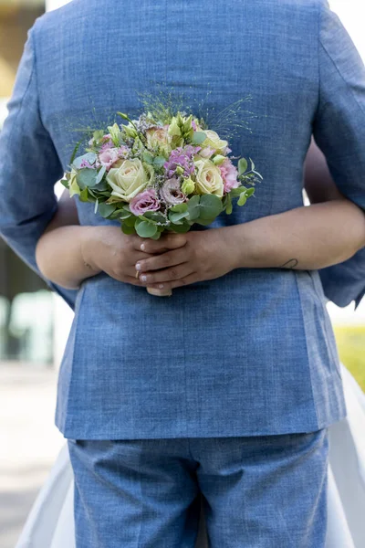 Крупным планом руки невесты с букетом белых и розовых роз, которые охватывают жениха синий жилет на фоне луга — стоковое фото