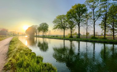 Nehir, ağaçlar ve çarpıcı gündoğumu yansımalarıyla sakin bir sabah sahnesi, doğal temalı ilham için ideal.