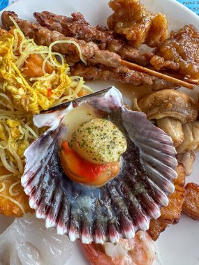 A vibrant and colorful seafood platter that features fresh scallops, grilled meats, and flavorful noodles