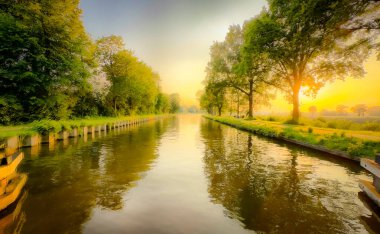 Gün doğumunda sakin bir nehir sahnesi, baş döndürücü doğayla huzur hissi için yumuşak yansımaları harmanlıyor.