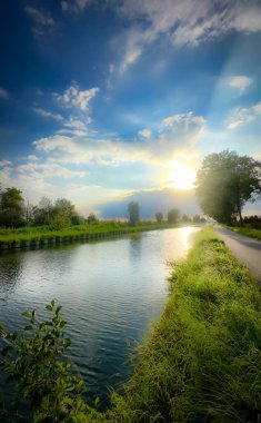 Huzurlu bir nehir manzarası sersemletici, büyüleyici bir gökyüzünün altında, yemyeşil, güzel bir şekilde kıyıları kaplıyor.