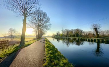Şafakta çok güzel sakin bir kanal sahnesi sergileniyor çarpıcı ağaçlar, güzel yansımalar ve canlı güneş ışığı.