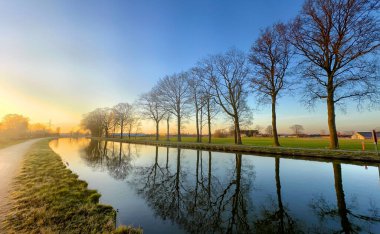 Sersemletici bir gündoğumu altında, güzel yansıtan, dingin, sakin bir kanal manzarası.