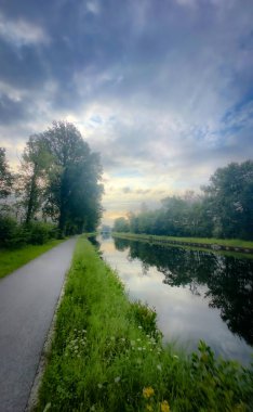 Canlı yemyeşil suların ve nazikçe yansıtan suların sardığı güzel, sakin bir kanal kenarı yolu.
