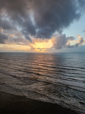 Güzel, sakin bir günbatımı sahnesi, okyanus dalgaları üzerine altın bir ışık yansıtıyor dramatik, dalgalı bulutlar altında