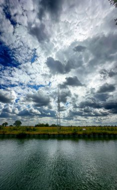 Kanal, dinamik kümülüs ve altostrat katmanlarının üzerinde dramatik bir kontrastla, yansıtıcı suyla süzülen devasa bulut oluşumları.