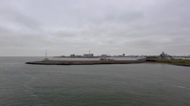 Den Helder, Hollanda, 25 Ekim 2024, uzak kıyılarda dalgakıran, endüstriyel liman binaları ve vinçlerle bulutlu liman silueti,