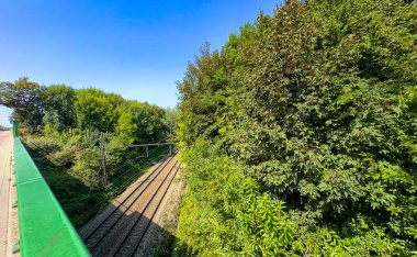 Demiryolu rayları yukarıdan görülüyor. Yeşil koridoru keserek geçiyor. Endüstriyel, doğa ile buluşuyor.,