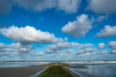 Huzurlu kıyı şeridi, aynalı havuzların ve bulutların arasında yürür, kıyı kenarındaki sakin patikada parıldayan kumlar ve geniş gökyüzü