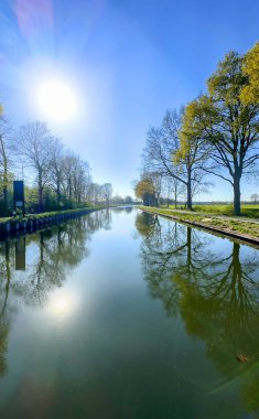 Ağaçları ve güneş ışığını yansıtan sakin bir kanal sahnesi, doğa ve manzara fotoğrafçılığı için mükemmel.