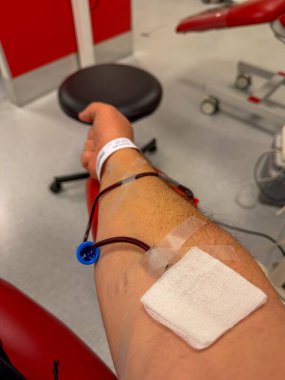 Kan bağışı iğnesi olan bir kol, tahsilat torbasına bağlı bir boru, delinme yerine yapıştırıcı sargı, yaslanmış bir donör.