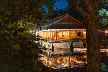 Altın yansımalı sakin deniz kenarı mekanı, Alacakaranlıkta aydınlatılmış Idyllic göl manzaralı pavyon davetkar