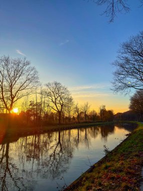 Altın Kanal Günbatımı Siluetli Ağaçlar ve Sıcak Yansımalar, Sakin Su Aynası ve Yumuşak Alacakaranlık Tonlarıyla,
