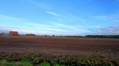 Rijkevorsel, Antwerpse Kempen, Belçika, akşam, traktör ve kırmızı kamyonla ovalanmış, ufukta kırmızı çiftlik evi, uzun mavi bulutlu derin mavi gökyüzü, ılık düşük ışık